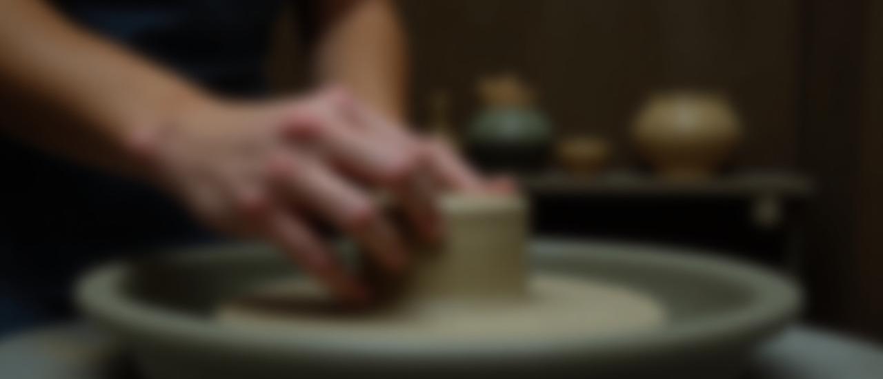 Künstlerhand formt Ton auf einer Töpferscheibe, umgeben von Keramikwerkzeugen und natürlichen Materialien.